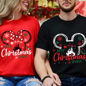 May include: A red t-shirt and a black t-shirt, each featuring a graphic of a mouse ear silhouette filled with snowflakes, a castle, and a Santa sleigh. The text "BEST Christmas EVER" is printed in white and red lettering on the shirts.