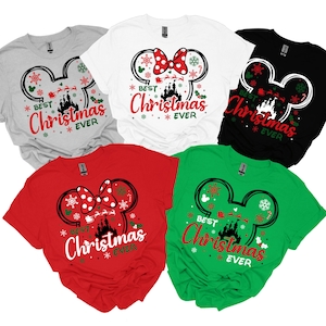 May include: Five short-sleeved t-shirts in gray, white, black, red, and green. Each shirt features a graphic of a Mickey Mouse ear silhouette containing a castle, Santa's sleigh, and snowflakes, with the text "BEST Christmas EVER" printed below.