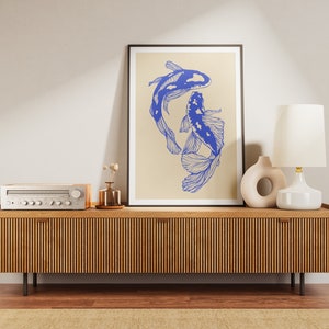 Pode incluir: Um console de m&iacute;dia de madeira com acabamento em madeira clara e ranhuras verticais. Um abajur branco com uma c&uacute;pula branca fica no console, ao lado de uma escultura de cer&acirc;mica. Uma impress&atilde;o emoldurada de dois peixes azuis em um fundo bege fica pendurada na parede acima do console.
