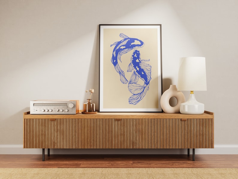 Pode incluir: Um console de m&iacute;dia de madeira com acabamento em madeira clara e ranhuras verticais. Um abajur branco com uma c&uacute;pula branca fica no console, ao lado de uma escultura de cer&acirc;mica. Uma impress&atilde;o emoldurada de dois peixes azuis em um fundo bege fica pendurada na parede acima do console.