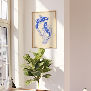 Pode incluir: Uma impress&atilde;o emoldurada de dois peixes koi azuis nadando em um design estilizado sobre um fundo creme. A impress&atilde;o est&aacute; pendurada em uma parede branca.