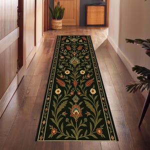 May include: A long, rectangular black runner rug with a floral pattern. The rug features a central design of stylized flowers and leaves in shades of red, green, and yellow, framed by a cream-coloured border. The rug is placed in a hallway.