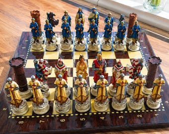 May include: A chess set featuring hand-painted resin pieces on a polished wooden board. One side features blue-clad figures and brown towers, while the other side displays cream-colored crusader-style figures with red crosses and brown towers.