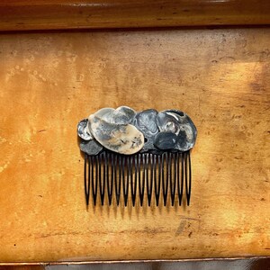 May include: A black plastic comb with a decorative design of black and white seashells. The comb has 11 teeth.