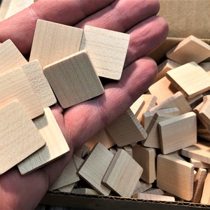 May include: A box filled with small, unfinished, square wooden blocks. The blocks are light brown in color and appear to be made of maple wood.