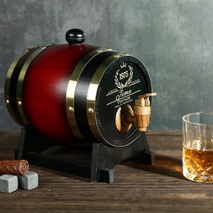 May include: A small wooden barrel with a black and gold band, a spigot, and a label that reads "1975 Limited Edition Time Vintage Made to Perfection". The barrel is sitting on a wooden stand and there is a glass of amber liquid next to it.
