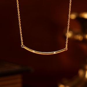 Peut inclure: Un collier en or délicat avec un pendentif en forme de barre incurvée. Le pendentif est orné de trois petites pierres précieuses scintillantes. Le collier est suspendu à une fine chaîne en or, créant un design élégant et minimaliste.