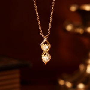 May include: A gold necklace with a pendant featuring two intertwined hearts set with clear cubic zirconia stones.