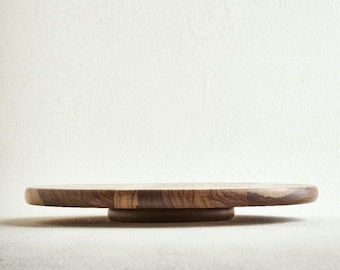 May include: A circular wooden lazy susan featuring a rich brown grain pattern with visible natural wood textures. The rotating serving tray has a smooth, flat top surface and is supported by a smaller, centered circular base underneath.