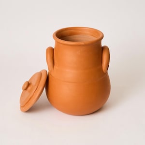 May include: A terracotta clay jar with a rounded body, a wide opening, and two side handles. The jar features a smooth, matte finish in a warm orange-brown hue. A matching circular lid with a small central knob is placed beside the jar.
