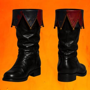 May include: A pair of black mid-calf boots featuring a decorative fold-over cuff. The cuff is designed with alternating dark blue and red triangular points, each accented with a small metallic bead at the tip, creating a distinct layered appearance.