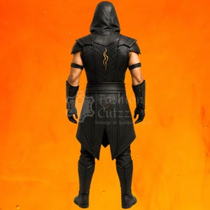 Puede incluir: Disfraz de cuero negro con una parte superior con capucha, armadura para los hombros y una t&uacute;nica. La parte posterior del disfraz presenta un dise&ntilde;o dorado. El texto "Fashion Cuttz Indulge in leather art" es visible en la t&uacute;nica.