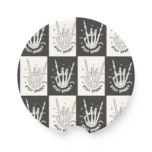 Op de afbeelding: Een ronde onderzetter met een zwart-wit geruit patroon. Het patroon bevat een skelethand die de rock-and-roll handbeweging maakt met de tekst "Stay Spooky" die overal wordt herhaald.