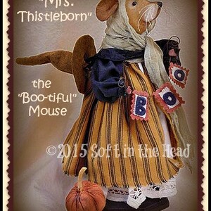 Peut inclure: Une poup&eacute;e souris artisanale, "Mrs. Thistleborn", v&ecirc;tue d'une robe ray&eacute;e orange et noire, d'un ch&acirc;le bleu et d'un foulard. La poup&eacute;e tient une banni&egrave;re "BOO" et a une petite citrouille. Le texte "the 'Boo-tiful' Mouse" est &eacute;galement visible.