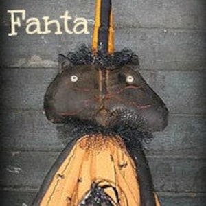 Pode incluir: Boneca de tecido preto com um chapéu de bruxa, uma máscara preta e um vestido preto e laranja. A boneca é etiquetada como "Miss Fanta".