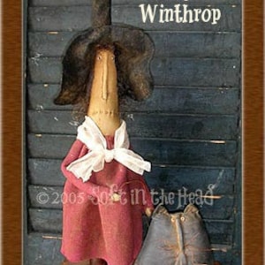 May include: Elvira Stump and Winthrop, a handmade rag doll witch with a black hat and a red dress, holding a black cat doll. The dolls are standing on a wooden surface with a sign that reads "Soft in the Head Patterns".