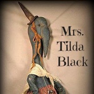 May include: A blue fabric doll with a long neck and a pointed hat. The doll is wearing a white dress and a red skirt. The doll is called "Mrs. Tilda Black".