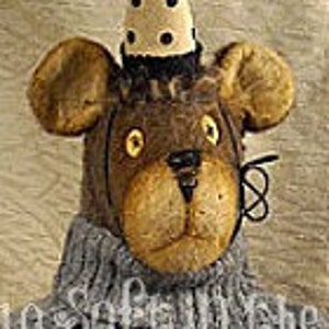 May include: A brown teddy bear wearing a gray sweater with a white and brown applique. The bear is wearing a white and black cone-shaped hat with black polka dots.