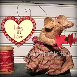 May include: A brown mouse doll wearing a red and brown plaid dress and holding two red hearts. The mouse is holding a red heart with the text "Lucy in Love" on it.