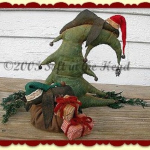 May include: A green felt Christmas tree with a brown felt hat and a red felt Santa hat. The tree is leaning to the side and has a brown felt bag with red and white felt presents at its base.