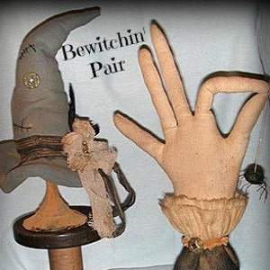 May include: A pair of witch-themed fabric crafts. One is a grey pointed hat with a black brim, brown straps, and a gold button. The other is a beige fabric hand with a brown cuff and a black spider.