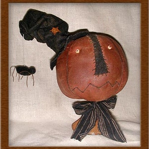 May include: A handmade pumpkin-shaped doll with a black felt hat and a black and white striped bow. The doll has a stitched-on face with black eyes and a black mouth. A small black spider hangs from the hat.