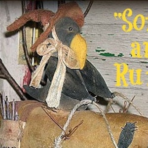 Może przedstawiać: Figurka drewnianego kruka w stylu folk art, w brązowym kapeluszu i beżowej kokardzie. Kruk ma żółty dziób i siedzi na beżowej powierzchni. Obraz zawiera tekst "Some are Rude".