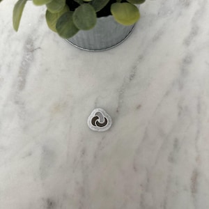 May include: A silver-colored metal charm in the shape of a heart with a swirl design.