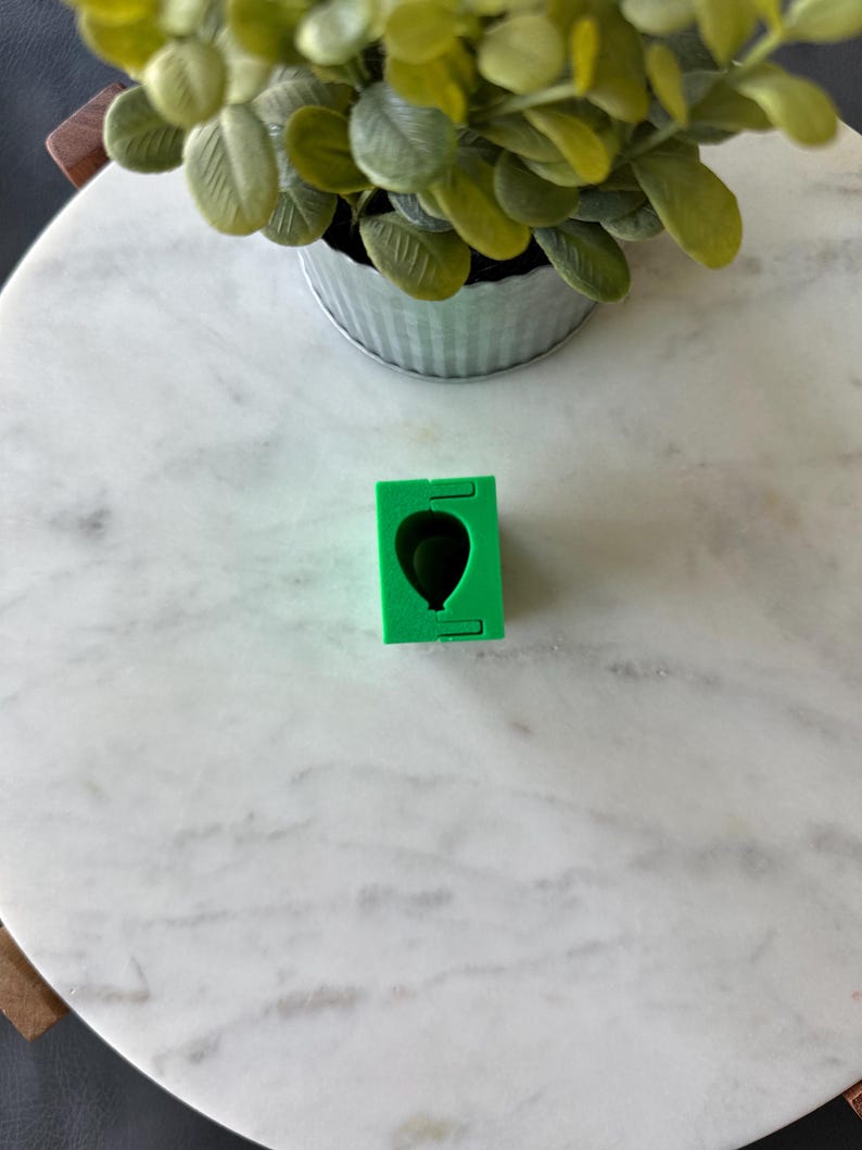 May include: Green silicone mould for making a balloon-shaped cake or other dessert. The mould is on a white marble surface.