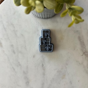 May include: A stack of three blue gift boxes with white ribbon and bow accents. The boxes are stacked on top of each other, with the largest box on the bottom and the smallest box on top.