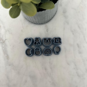 May include: A set of nine grey plastic cookie cutters in various shapes, including a heart, a horseshoe, a four-leaf clover, a rainbow, a pot of gold, a balloon, and a shamrock.