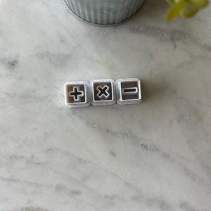 May include: Three white plastic cookie cutters shaped like the mathematical symbols plus, multiply, and minus.