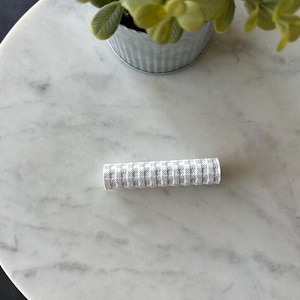 May include: A white and gray patterned rolling pin on a white marble surface.