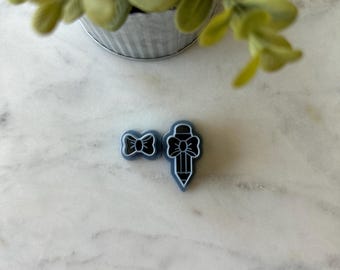 May include: Two blue resin cookie cutters, one shaped like a pencil with a bow on top and the other shaped like a bow.