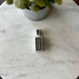 May include: White plastic cookie cutter shaped like a bottle with a lid. The cookie cutter is on a white marble surface.