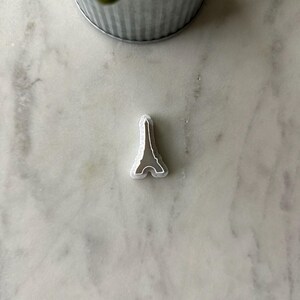 May include: A silver-colored metal cookie cutter shaped like the Eiffel Tower.