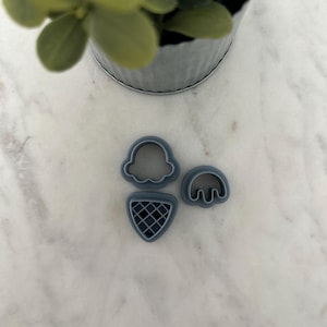 May include: Three blue plastic cookie cutters shaped like an ice cream cone, a scoop of ice cream, and a cherry.