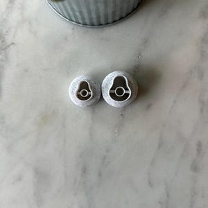 May include: Two white plastic avocado-shaped cookie cutters. The cutters are on a white marble surface.