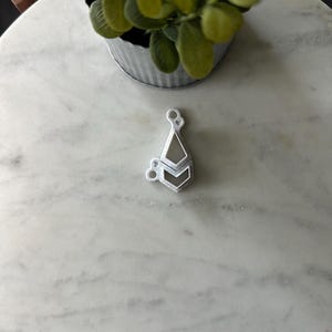 May include: A white metal pendant with a geometric design. The pendant is shaped like a double arrowhead and has a shiny finish.