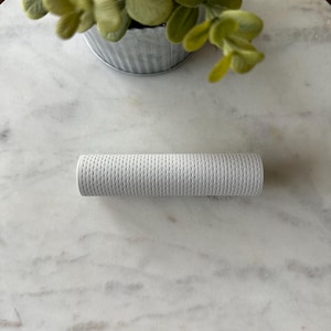 May include: A white, cylindrical, textured object with a repeating pattern of small holes. The object is sitting on a white marble surface.