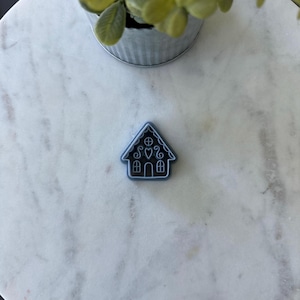 May include: A blue gingerbread house cookie cutter on a white marble surface.