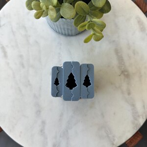 May include: Three gray silicone baking molds with a Christmas tree design. The molds are stacked on top of each other.