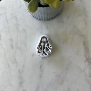 May include: White plastic cookie cutter shaped like a Christmas tree with a star on top and small circles cut out of the tree.