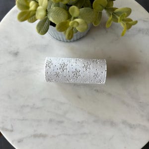 May include: White fabric roll with a snowflake pattern. The roll is on a white marble surface.