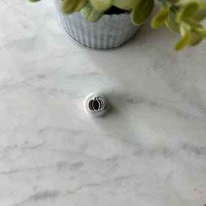 May include: A silver metal pumpkin-shaped cookie cutter on a white marble surface.