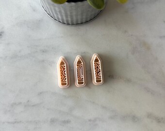 May include: Three beige pencil-shaped objects with decorative patterns and the word "Dream" printed on one. The objects are arranged on a white marble surface, with a small potted plant in the background.