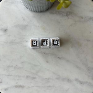 May include: Three white square blocks with the letters "a", "d", and "c" printed in black on the top of each block.