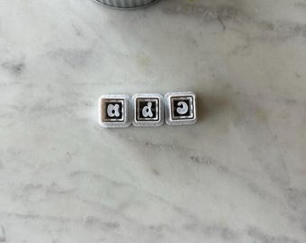 May include: Three white square blocks with the letters "a", "d", and "c" printed in black on the top of each block.