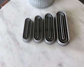 May include: Four silver metal cookie cutters in the shape of an oval. The cutters are arranged in a row from largest to smallest.
