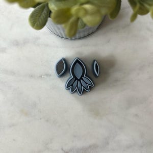 May include: A set of three blue silicone cookie cutters shaped like leaves. The cutters are on a white marble surface.